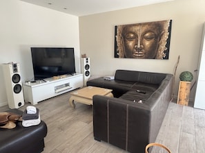 Una sala de estar moderna con un televisor de pantalla plana grande, un sofá de cuero negro, una mesa de centro de madera y una estatua de Buda en la pared.