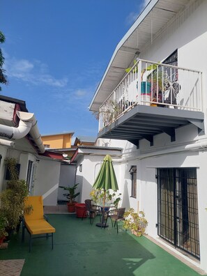 A courtyard with a green lawn, outdoor furniture, potted plants, and a white building with a balcony. - Breezy African Suite (Woodbrook)