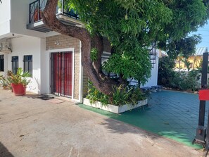 Un edificio residencial con un árbol grande en el patio, una puerta roja y plantas en macetas.