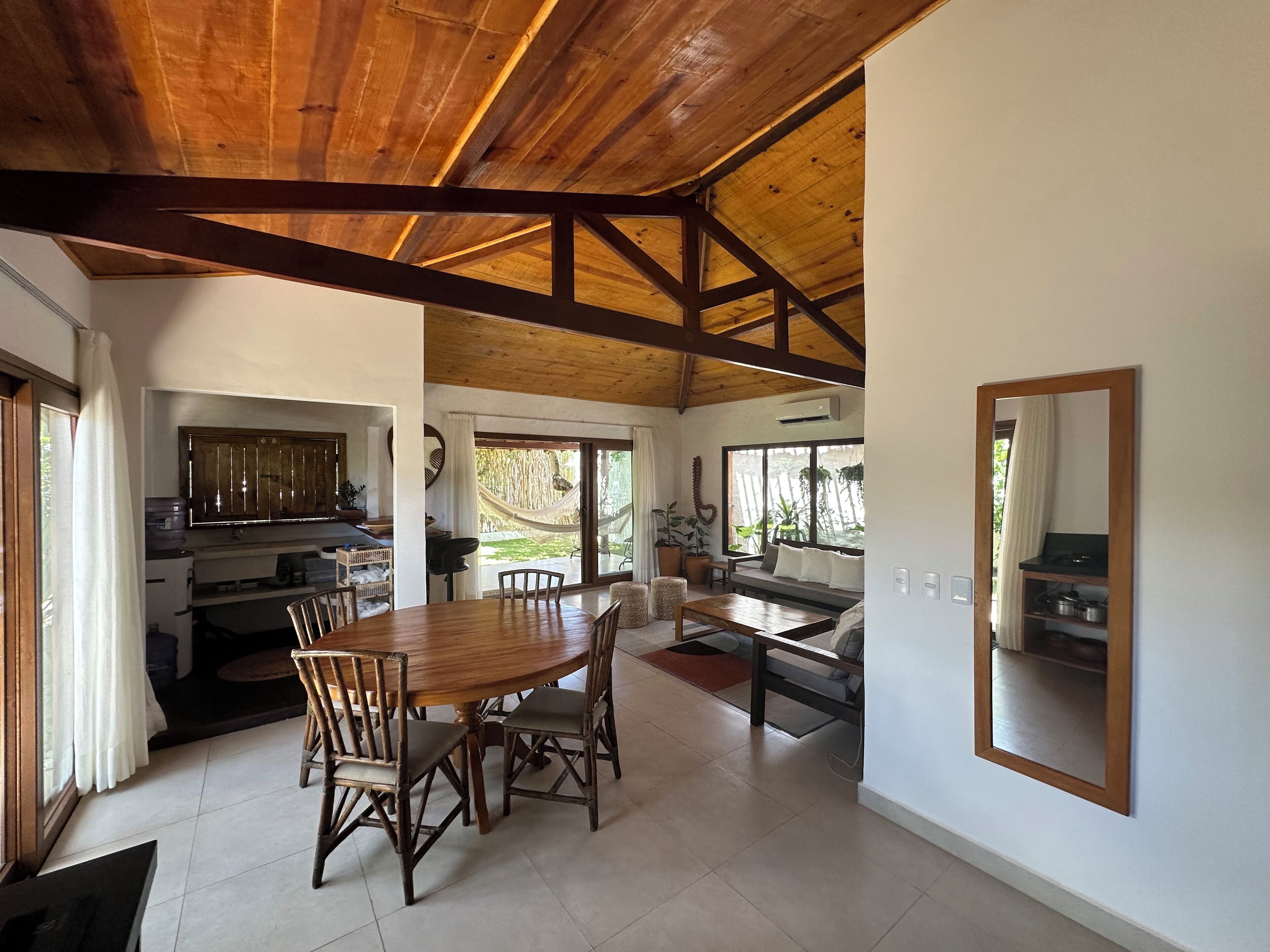 A spacious kitchen with a wooden ceiling, a dining area with a large table and chairs, and a view of the outdoors through large windows.