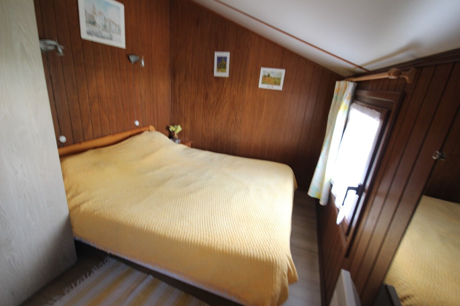 A small, cozy room with a single bed, wooden walls, and a small window with curtains.
