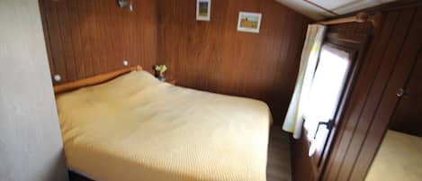 A small, cozy room with a single bed, wooden walls, and a small window with curtains.