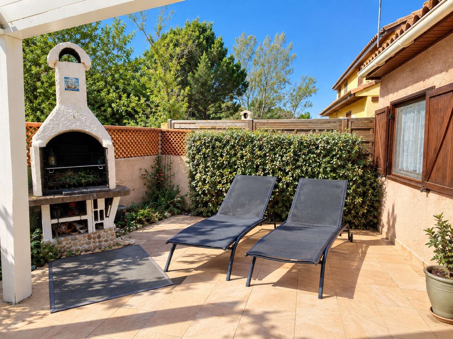 An outdoor patio with a barbecue grill, two lounge chairs, and a wooden fence.
