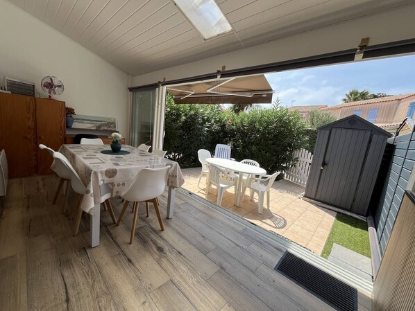 An open-plan living space with a dining area, a kitchen, and a patio with a view of the garden and neighboring houses.