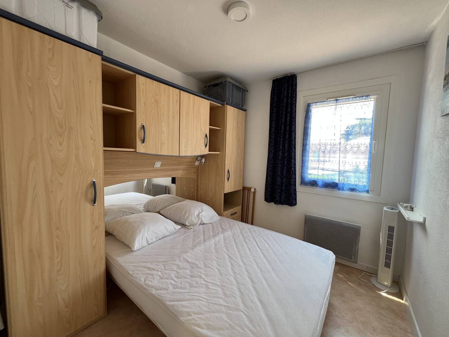 A bedroom with a bed, wooden wardrobe, and a window with curtains.