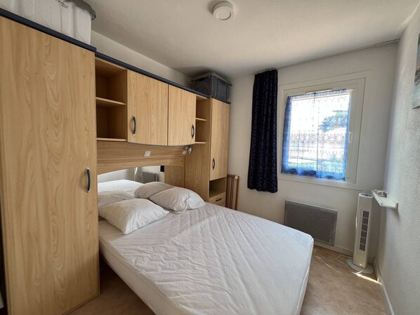 A bedroom with a bed, wooden wardrobe, and a window with curtains.
