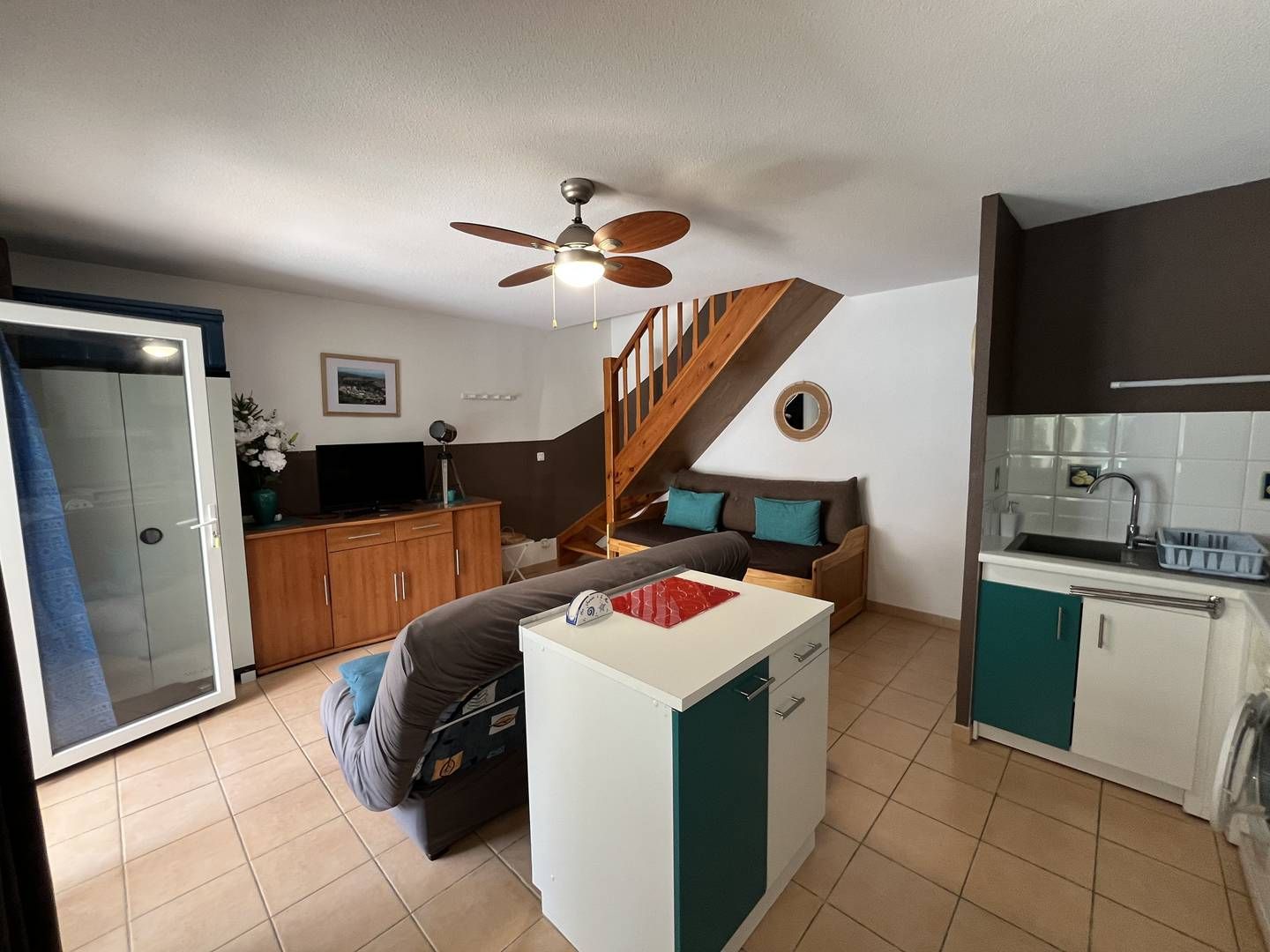 A compact living space with a kitchenette, a sofa, a small table, and a ceiling fan.