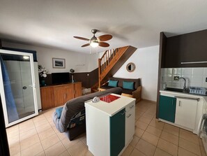A compact living space with a kitchenette, a sofa, a small table, and a ceiling fan.