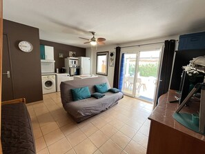A compact living space with a sofa, kitchenette, and a sliding glass door leading to an outdoor area.