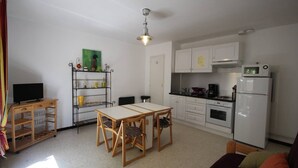 A compact living space with a kitchenette, a dining area with a table and chairs, a TV on a stand, and a bookshelf.
