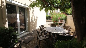 An outdoor patio with a round table and chairs, surrounded by plants and a tree.