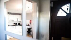 Visão através de uma porta para uma cozinha moderna com armários brancos, bancada preta e uma área de jantar com cadeiras.