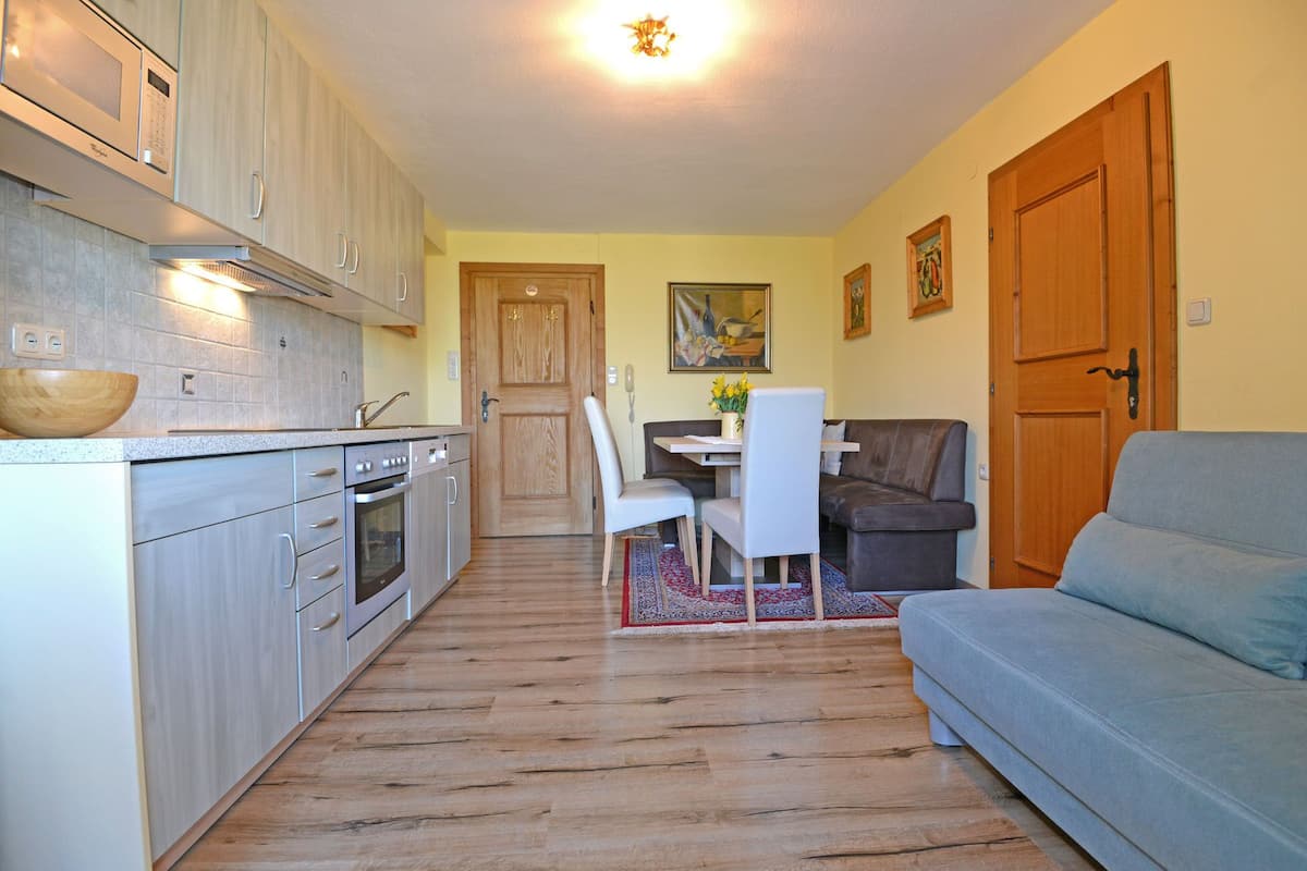 A compact kitchen with a microwave, oven, and sink, leading to a dining area with a table and chairs.