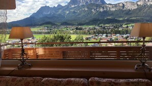 Un balcón con barandas de madera y dos lámparas, con vistas a un paisaje montañoso y un pueblo abajo.