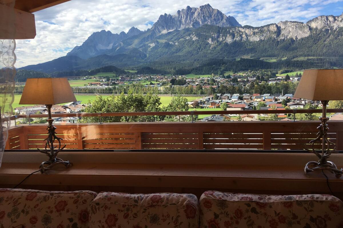 A balcony with wooden railings and two lamps, overlooking a mountainous landscape with a town below.