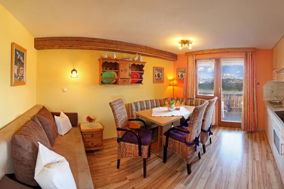 A cozy living room with a sofa, dining table, and chairs. There is a kitchen area with a sink and a telephone.