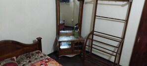 Un dormitorio con una cama de madera, una mesita de noche con espejo y un perchero metálico.