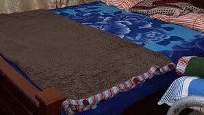 Quarto com cama de madeira, cortinas estampadas e colcha azul com flores.