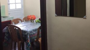 Uma sala de jantar com uma mesa posta para quatro pessoas, cadeiras e um vaso com flores.