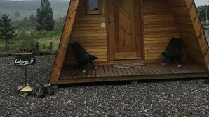 A wooden cabin with a pitched roof, a front door, and two benches outside. - Pousada Bolicho Guabiroba (Cambara do Sul)