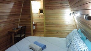 A cozy wooden cabin room with a bed, a chair, and a small table. - Pousada Bolicho Guabiroba (Cambara do Sul)