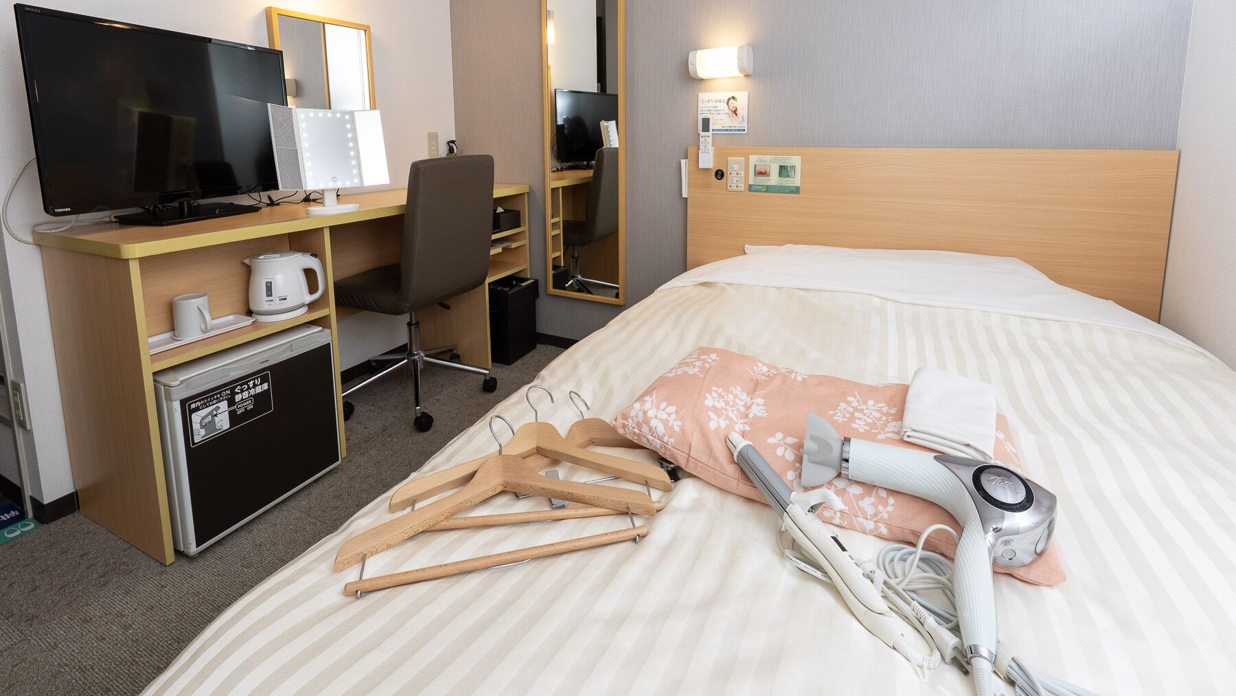 A hotel room with a bed, a desk with a computer, a television, and a mirror.