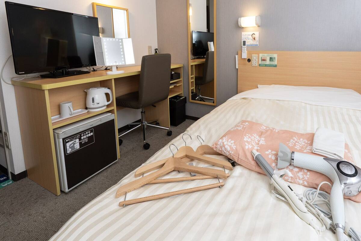 Una habitación de hotel con una cama, un escritorio con computadora, un televisor y un espejo.