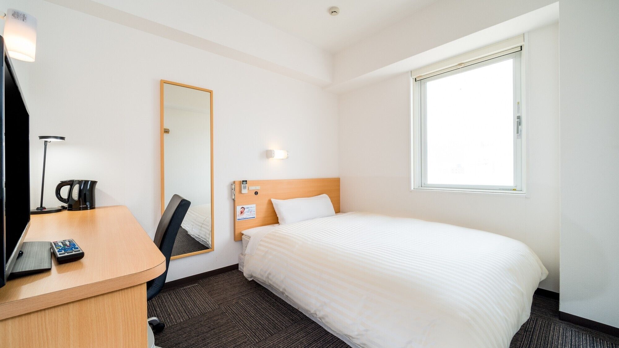 Een hotelkamer met een bed, een bureau met een lamp, een spiegel en een raam.