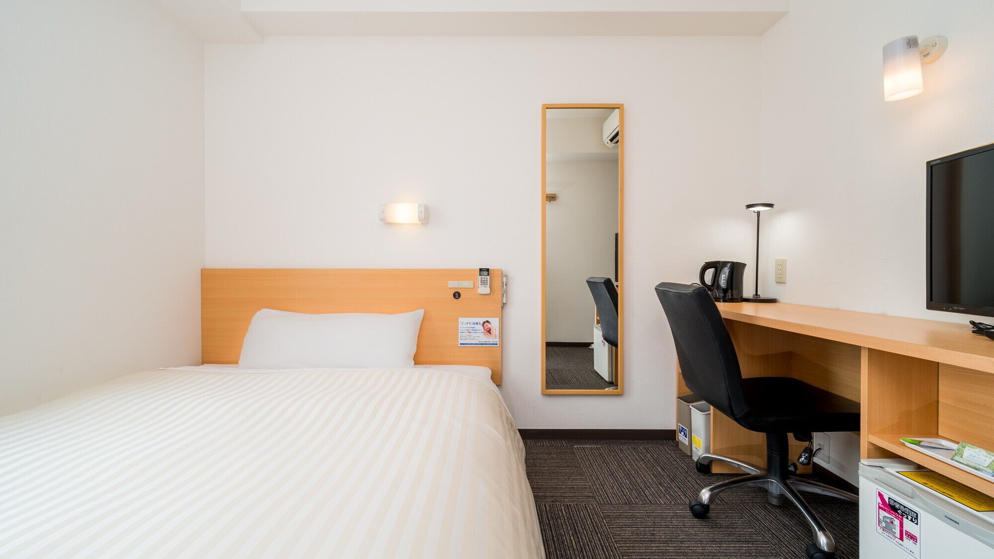 A hotel room with a bed, a desk with a chair, a television, and a mirror.
