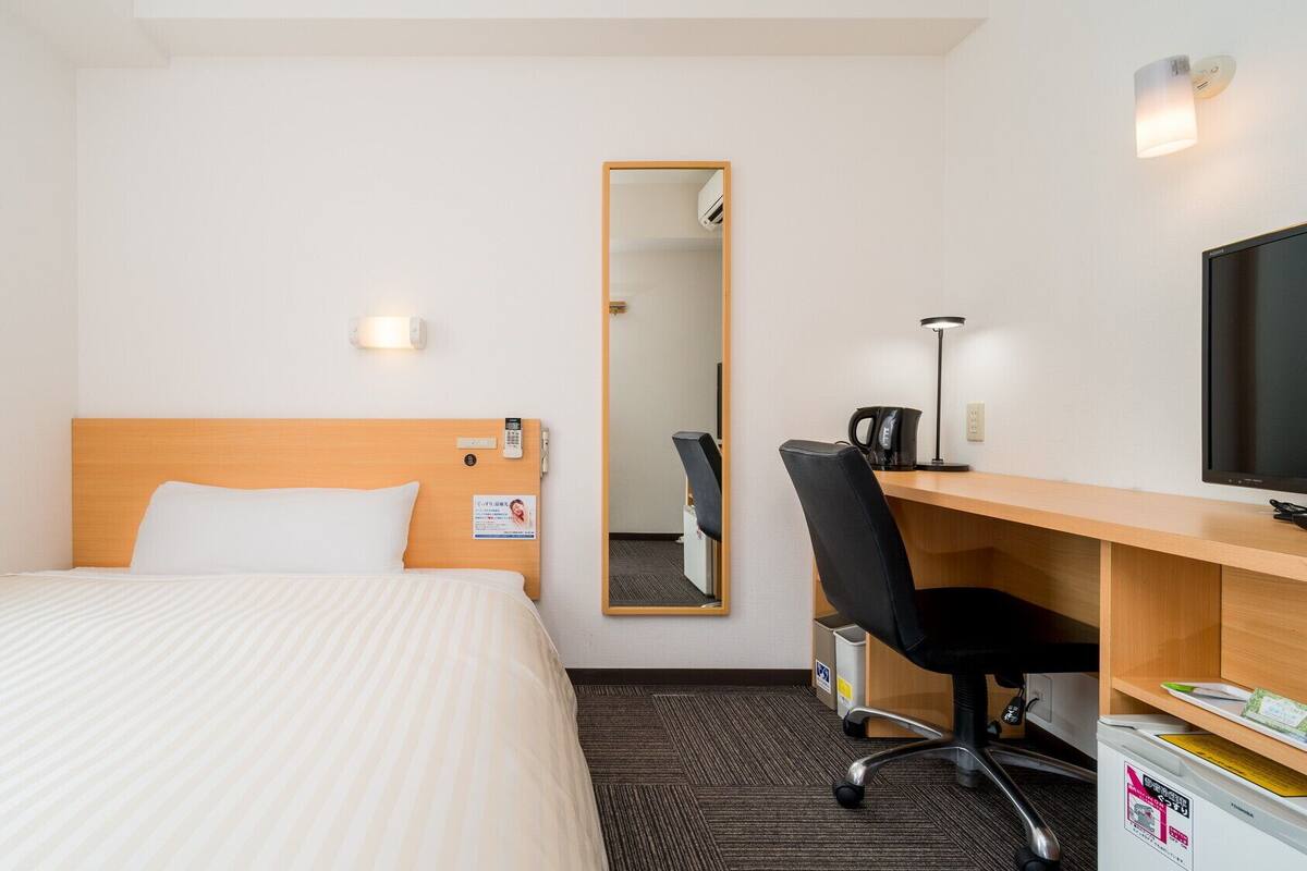 Una habitación de hotel con cama, escritorio, silla, televisor y espejo.