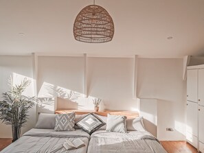 A bedroom with a bed, pillows, a hanging light fixture, a bedside table, and a potted plant. - Murals Hostel & Cafe Mactan (Lapu-Lapu)