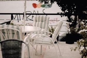 A patio area with white and green striped chairs around a round table, potted plants, and a sign with the word "MIRALS" partially visible. - Murals Hostel & Cafe Mactan (Lapu-Lapu)