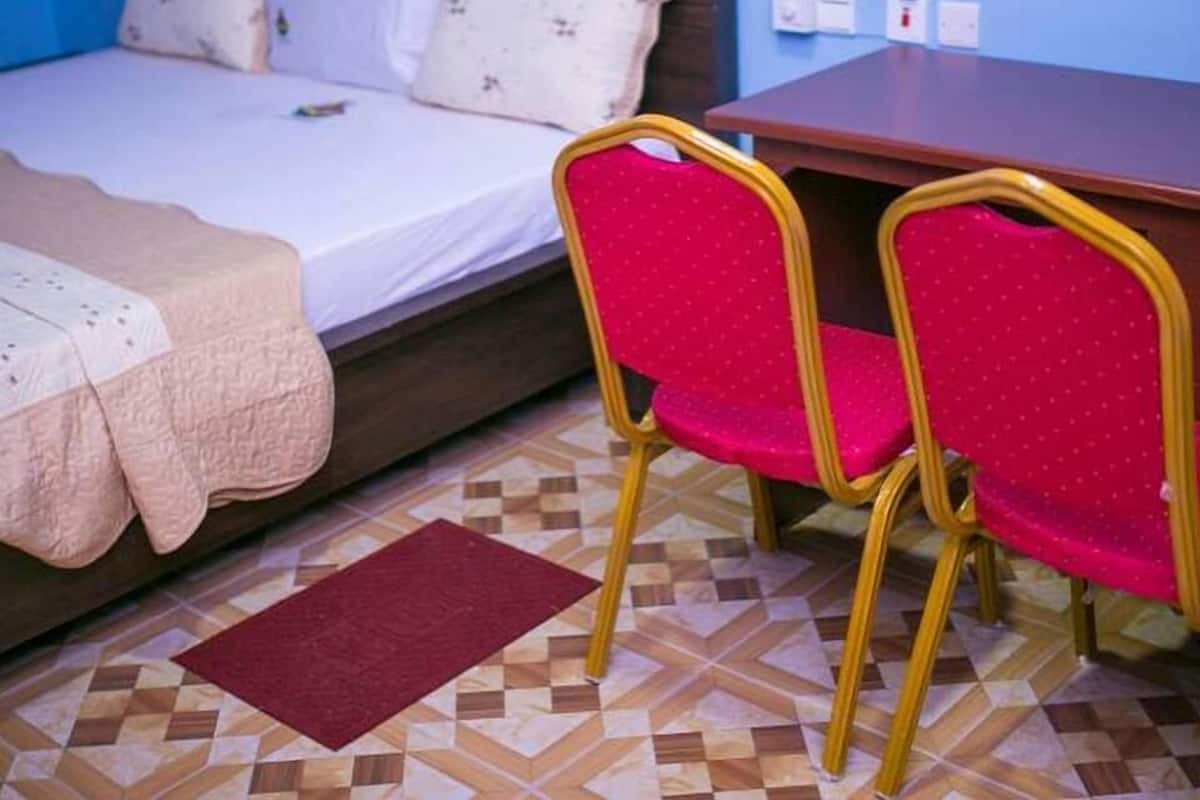 A bedroom with a bed, two pillows, a bedside table, and a chair.