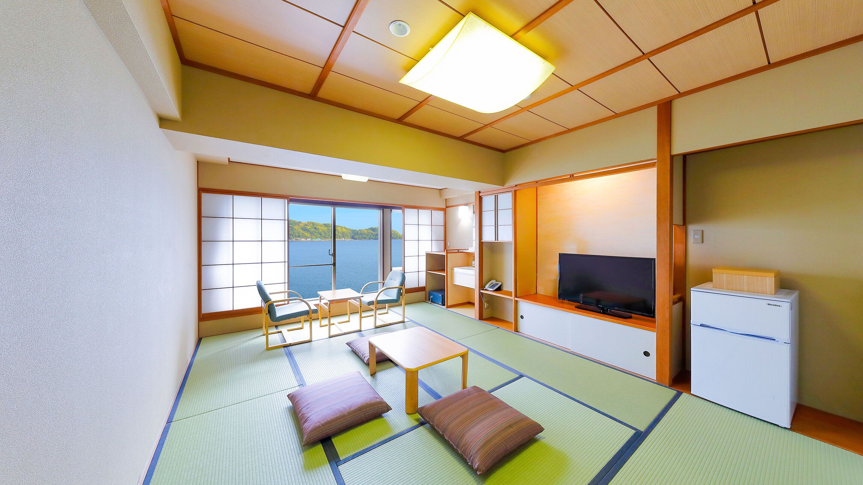 Ein traditioneller japanischer Raum mit Tatami-Böden, einem Fernseher, einem Kühlschrank und Meerblick.