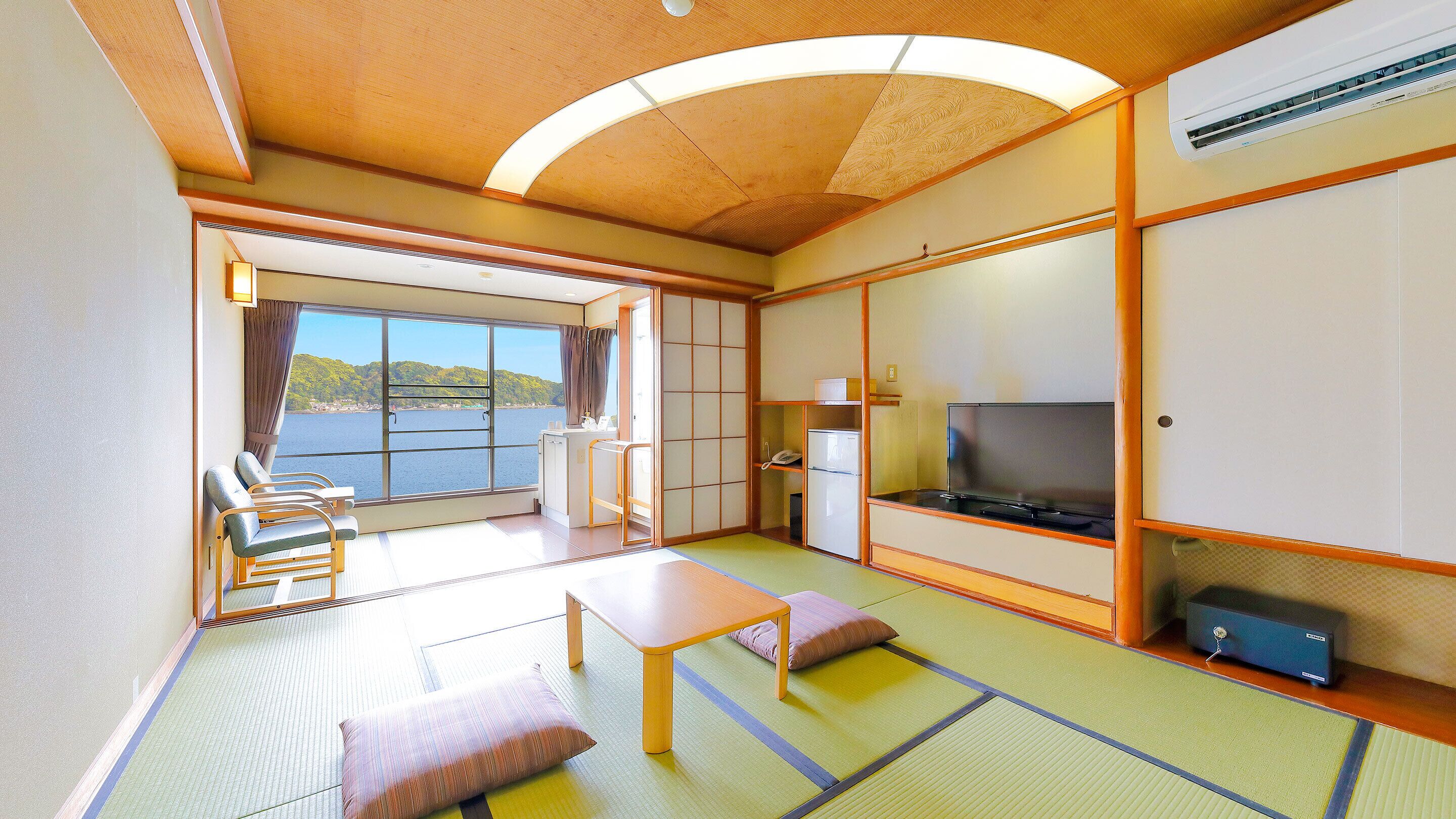 Ein Zimmer mit Tatami-Böden, einem Fernseher, einem Kühlschrank und Blick aufs Meer.