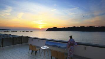A balcony with a table and chairs, overlooking a body of water at sunset.