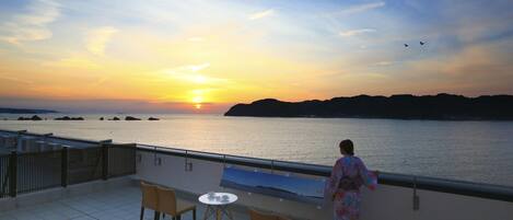 A balcony with a table and chairs, overlooking a body of water at sunset.