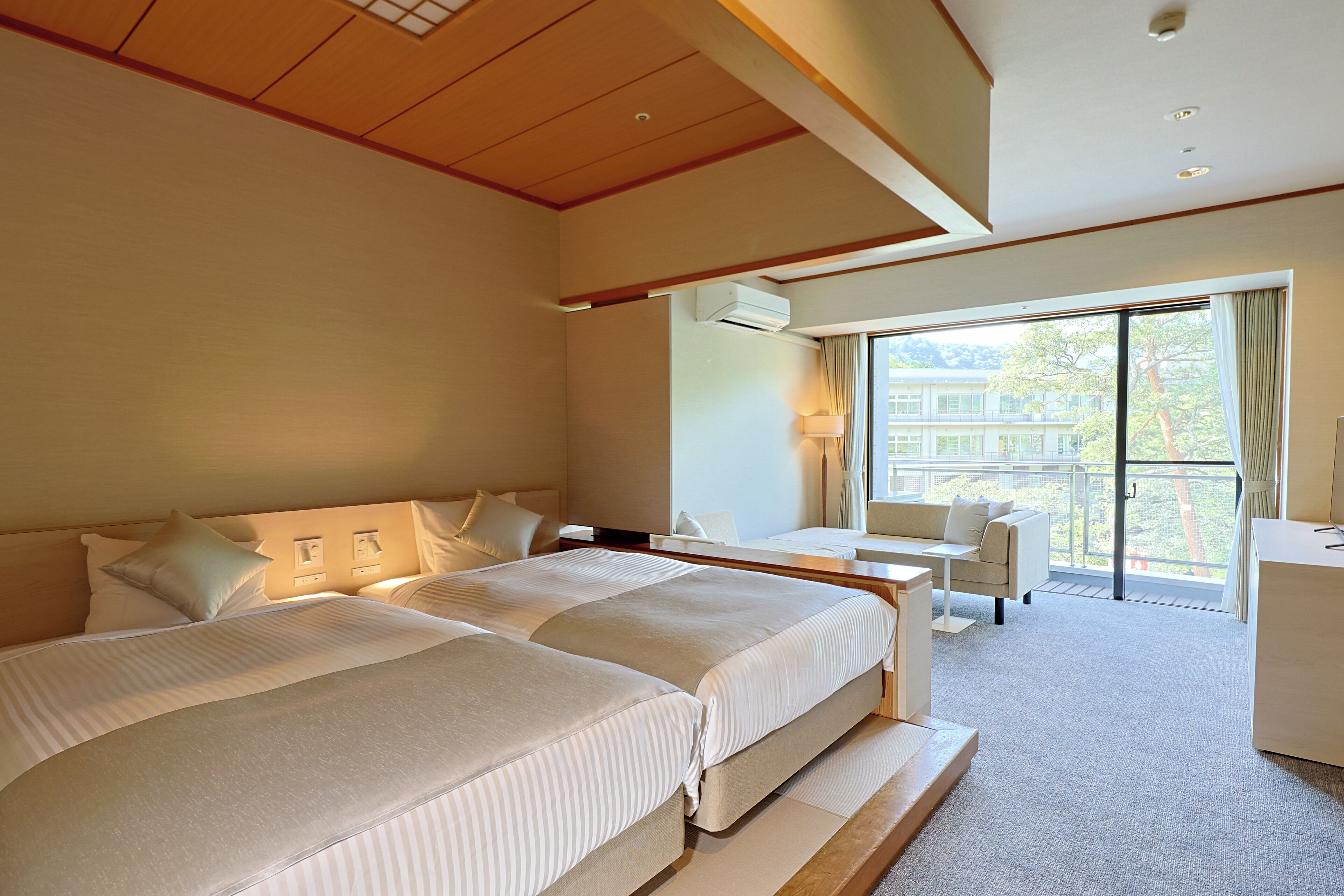 Hotellihuone, jossa on kaksi sänkyä, työpöytä ja parveke, jolta on näkymä rakennuksiin.