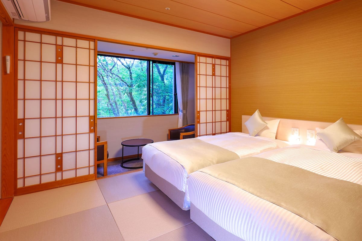 Une chambre de style japonais traditionnel, avec un sol recouvert de tatamis, un grand lit avec une literie blanche et une porte coulissante en papier de riz (shoji).