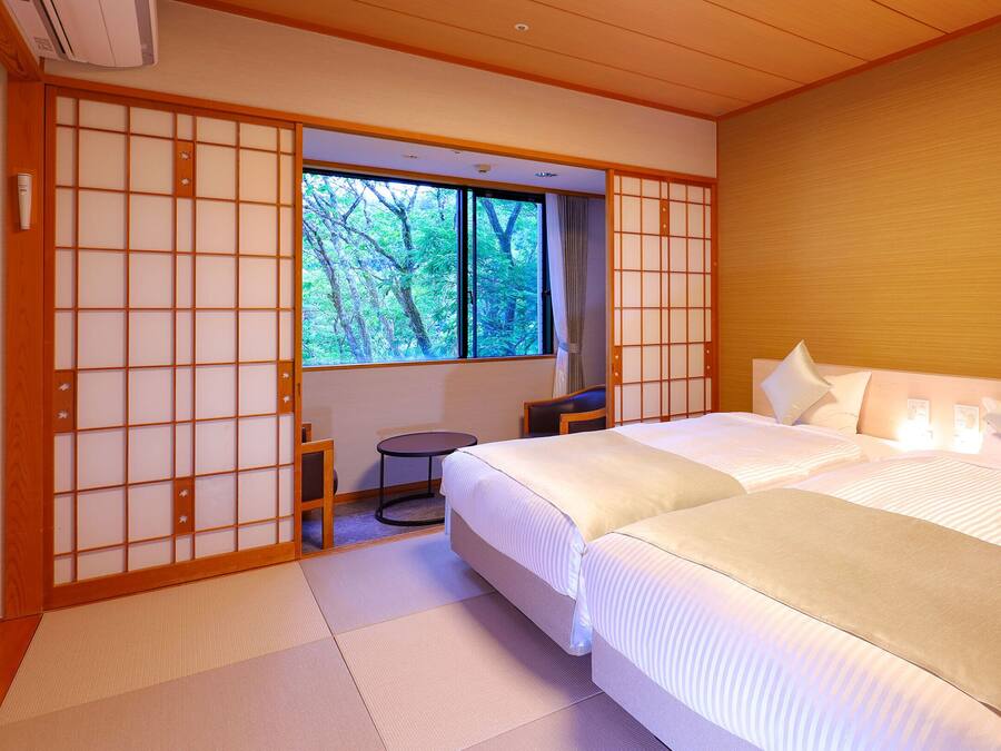 Un dormitorio en estilo japonés tradicional, con suelo de tatami, una cama grande con ropa de cama blanca y una puerta corrediza tipo shoji.