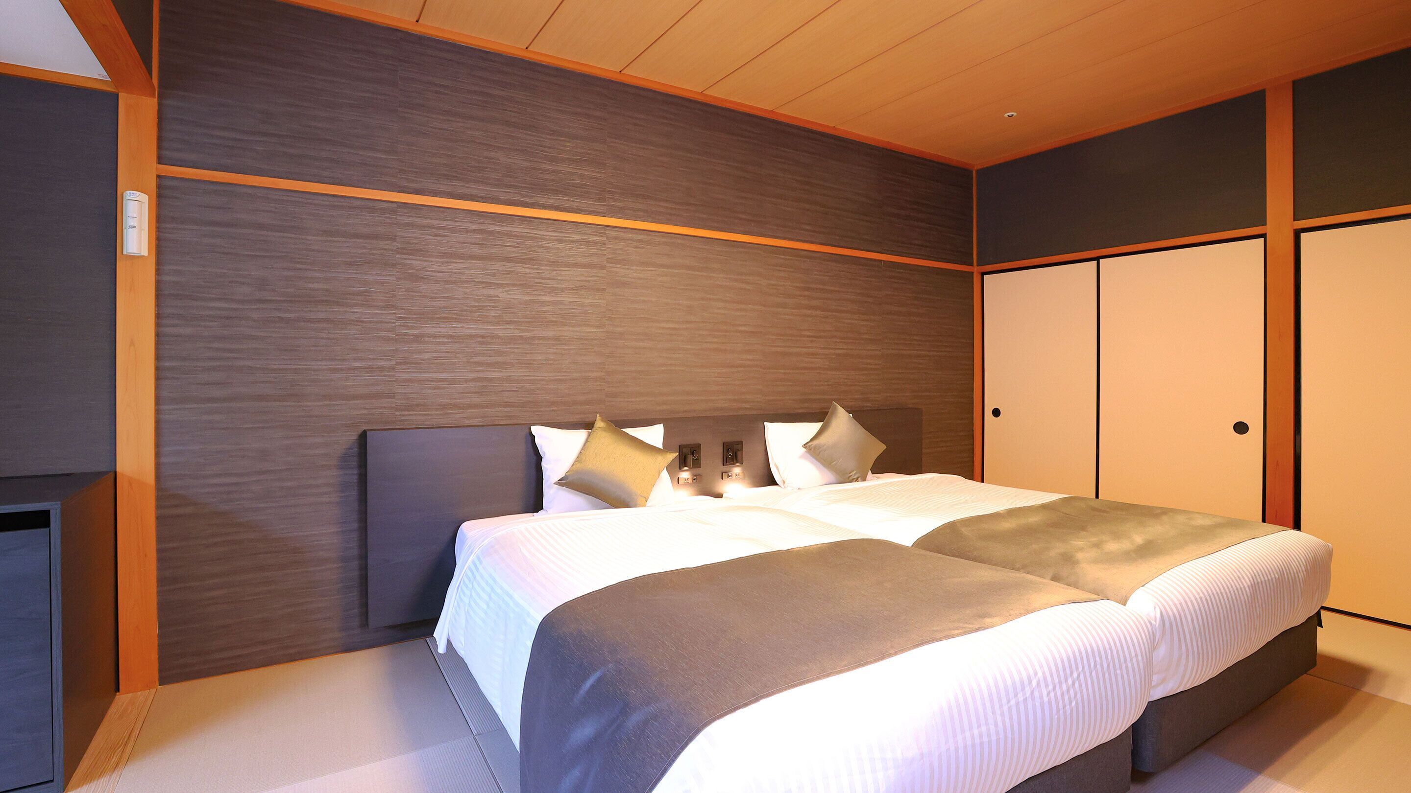 Une chambre d’hôtel moderne avec un grand lit, une tête de lit en bois et une armoire intégrée.
