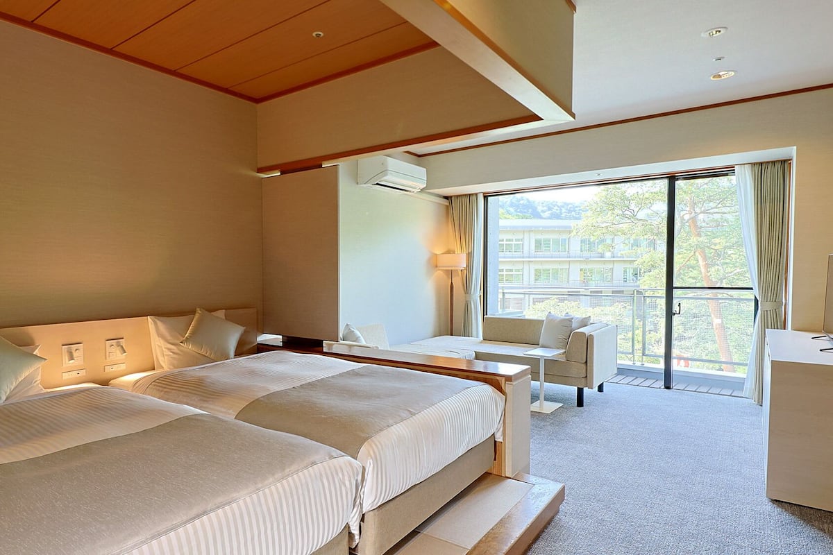 Une chambre d’hôtel avec deux lits, un bureau, une chaise et un balcon avec vue.