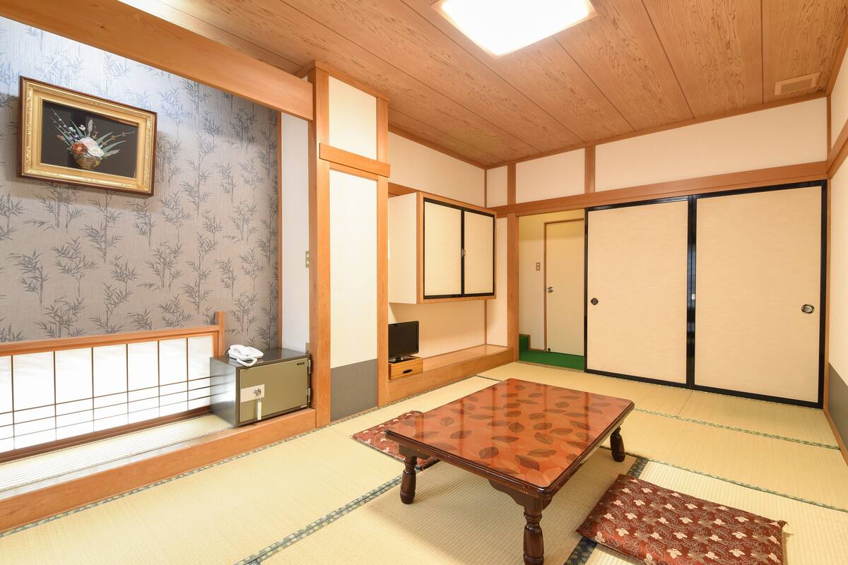 A traditional Japanese room with tatami flooring, a low wooden table, sliding doors, and a framed picture on the wall.