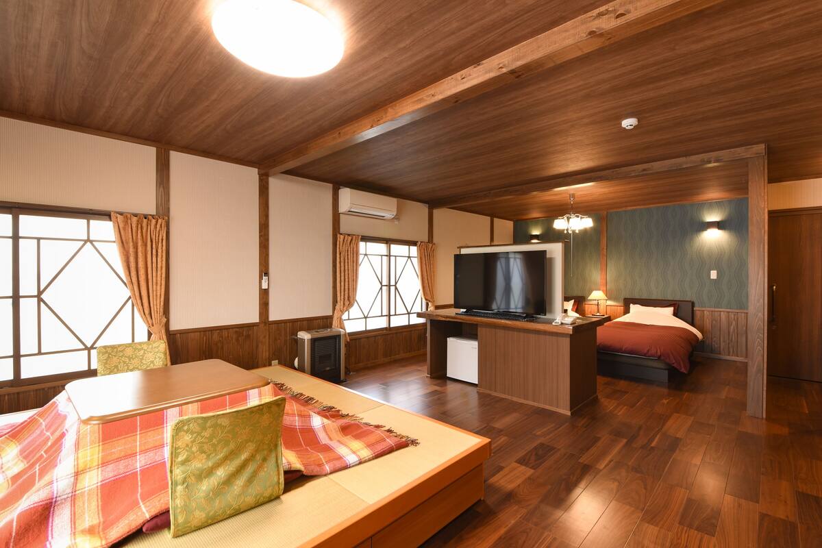 A room with a bed, a desk with a TV, a chair, and a window with curtains.