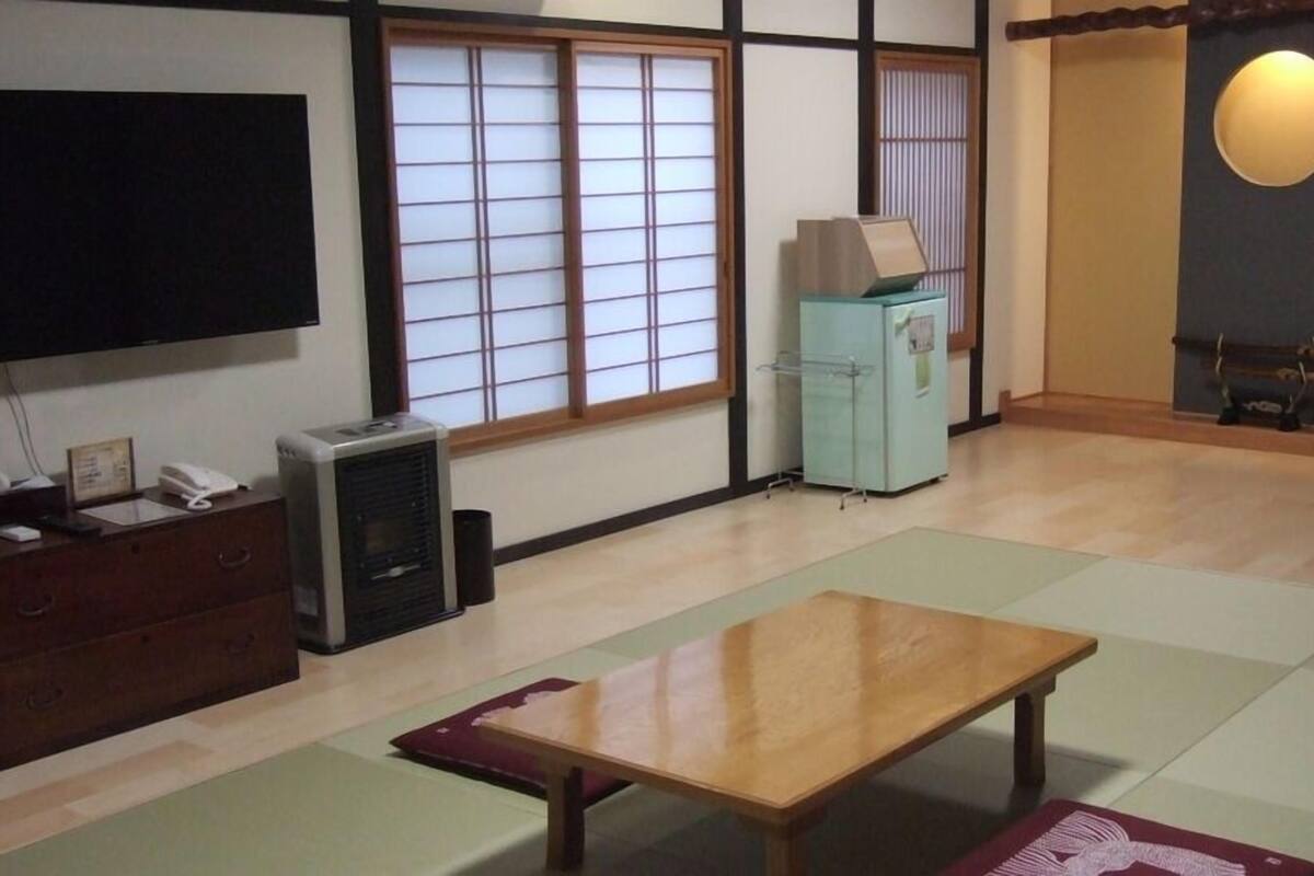 A traditional Japanese-style room with tatami flooring, a television, a heater, and a cabinet.