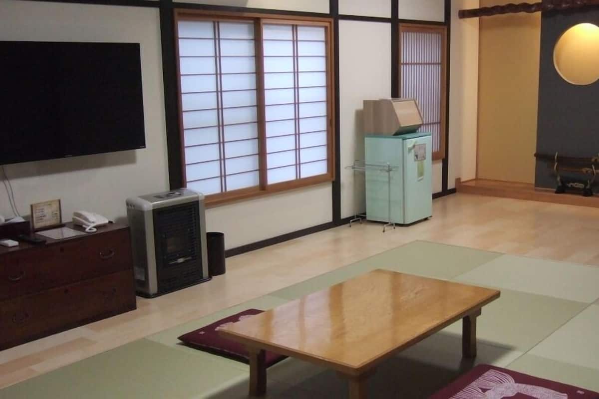 A traditional Japanese-style room with tatami flooring, a television, a heater, and a cabinet.