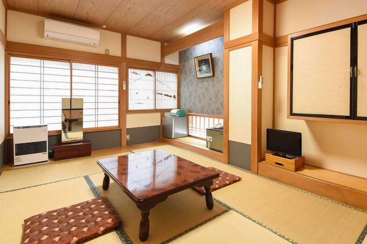 A traditional Japanese room with tatami flooring, a low table, sliding doors, and a TV on a wooden stand.