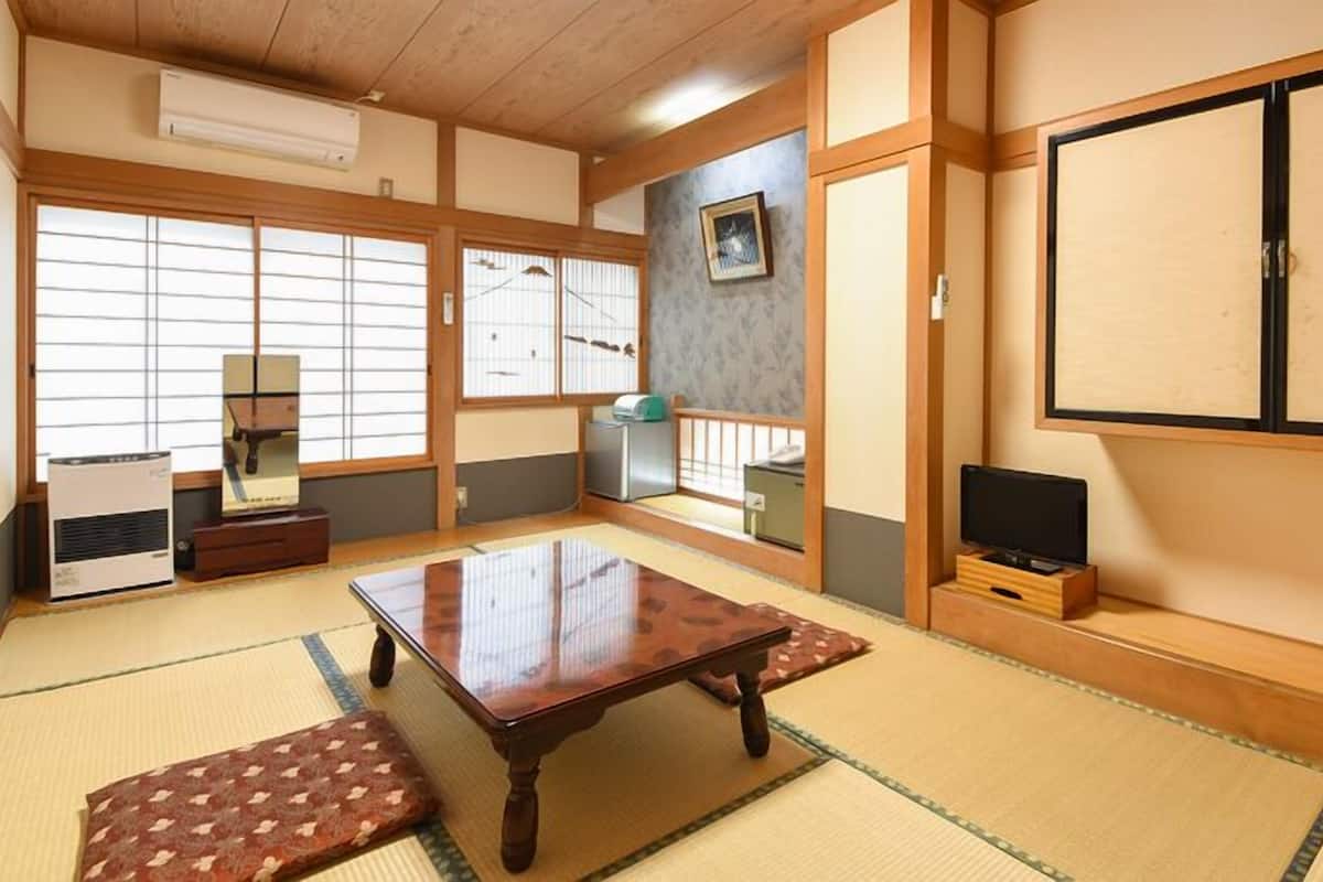 A traditional Japanese room with tatami flooring, a low table, sliding doors, and a TV on a wooden stand.