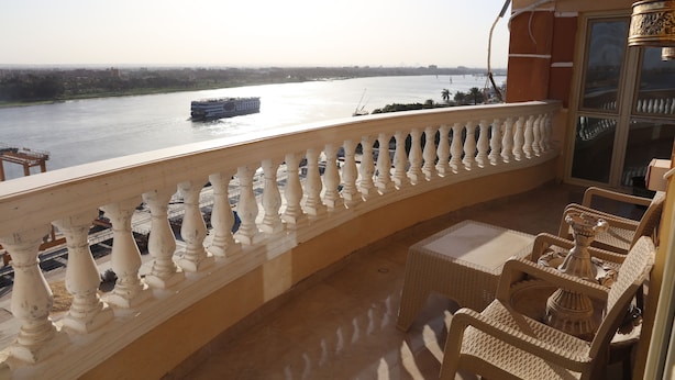 A balcony with a view of a river and a boat. There are wicker chairs and a table. - Luxurious and Panoramic Nile view. (Cairo)