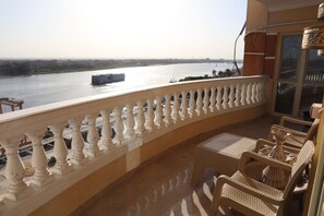 A balcony with a view of a river and a boat. There are wicker chairs and a table. - Luxurious and Panoramic Nile view. (Cairo)